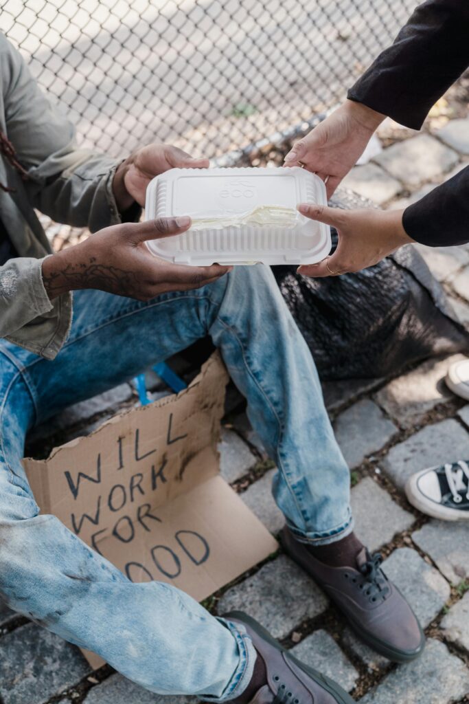 A compassionate act of giving food to a homeless person sitting on a city sidewalk.